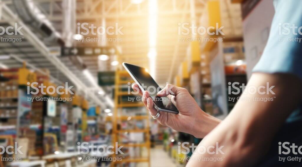 Factory worker using application on mobile smartphone to operate automation for modern trade. Checking order in large warehouse. Import and export the shipping cargo.