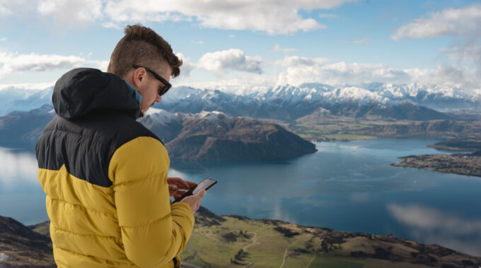 Man With Using Smartphone In Mountain Summit. Roy's Peak, Wanaka, New Zealand Landscape