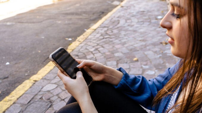 Close Up Of A Relaxed Girl Checking Mobile Phone On Line Sitting On A Street